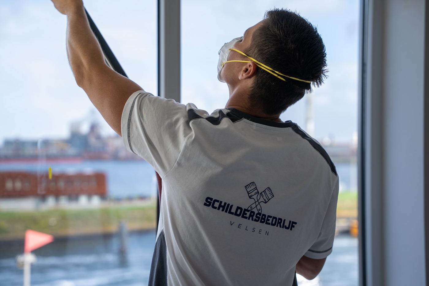 Schilder plakt een kozijn af, met uitzicht op de haven