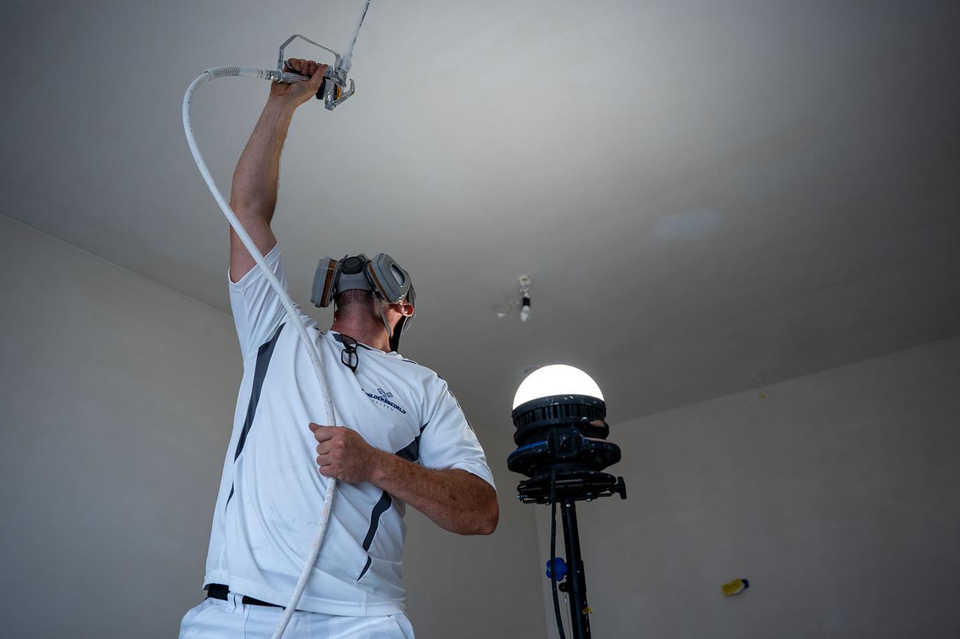 Schilder spuit een plafond met latex, werklamp op de achtergrond